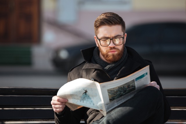 Man reading a business newspaper on a bench